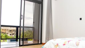A bedroom with a large sliding glass door leading to a balcony, a bed with a colorful feather-patterned duvet, and a white wall. - K&K Luxurious Landing (Limbe)