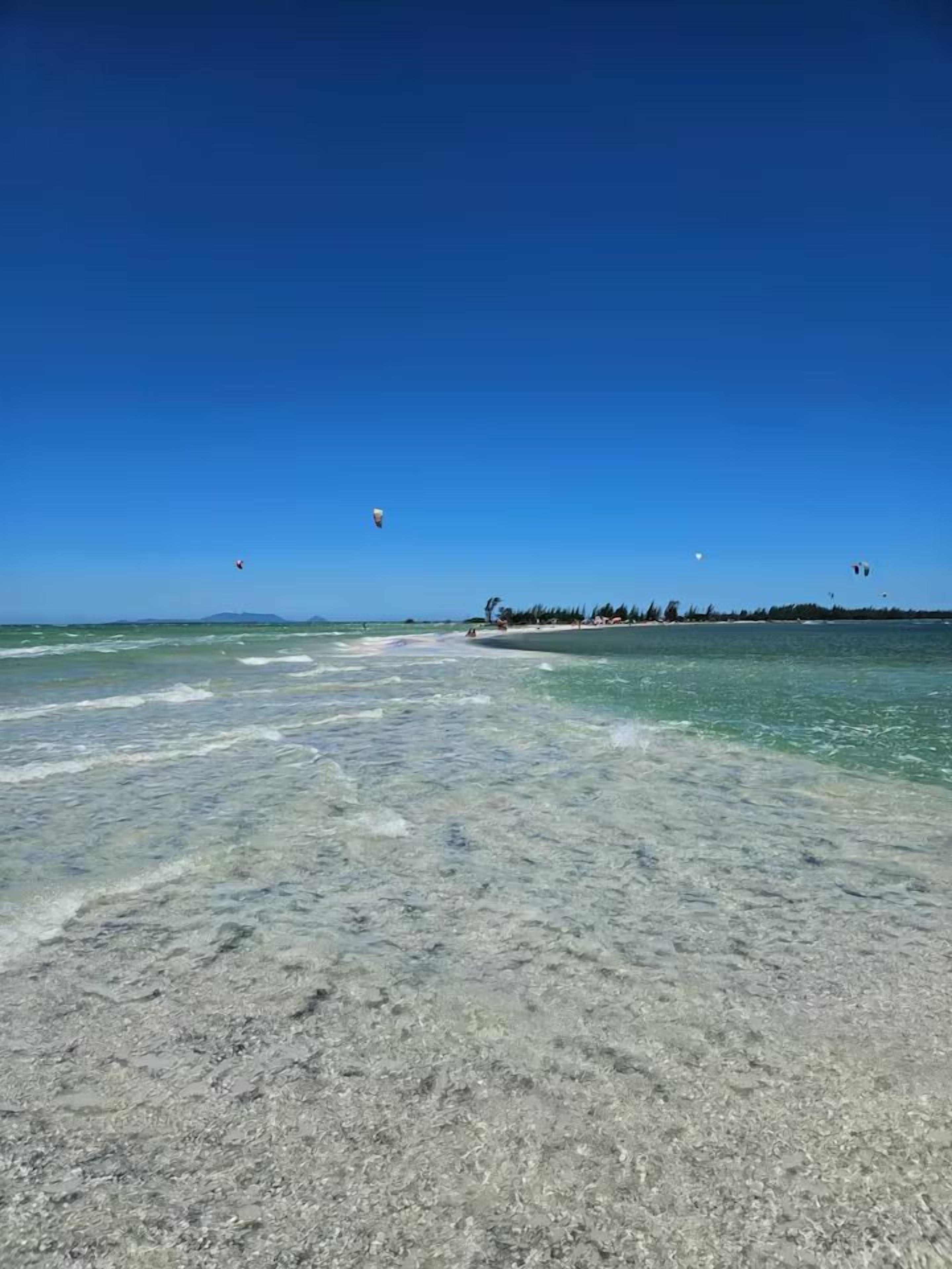 Una playa con agua cristalina, una orilla arenosa y una costa distante con vegetación.