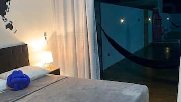Una habitación de hotel con cama, mesita de noche, lámpara, un mapa del mundo en la pared y vistas al exterior a través de una puerta de cristal.