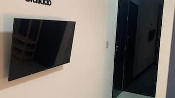 Um corredor com televisão de tela plana presa na parede, uma porta e um lustre no teto.