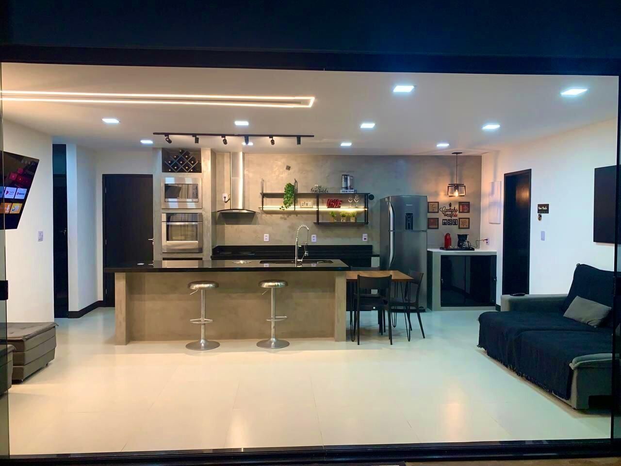 Una cocina moderna con una isla central, taburetes de bar y un comedor con sofá y mesa.