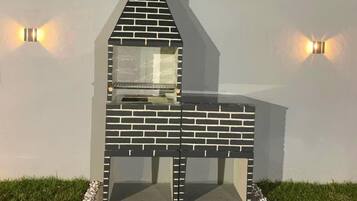 Una parrilla de ladrillo con chimenea, frente a una pared blanca con dos luces empotradas.