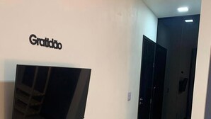 A hallway with a flat-screen TV mounted on the wall, a door, and a light fixture on the ceiling. - CASA PREMIUM - ARRAIAL DO CABO - RJ (Arraial do Cabo)