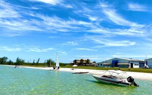 Una playa con aguas cristalinas, un velero y un edificio con techo azul.