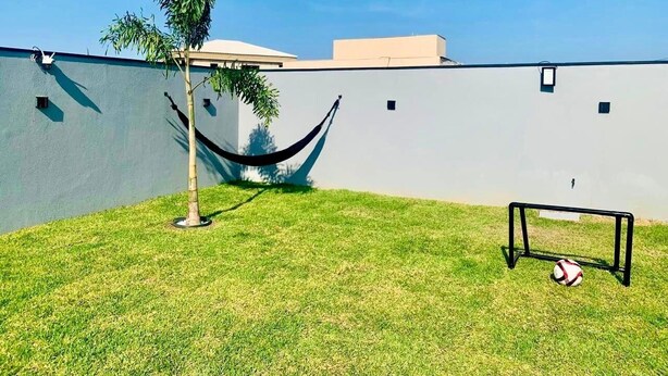 A grassy area with a hammock, a soccer goal, and a wall. - CASA PREMIUM - ARRAIAL DO CABO - RJ (Arraial do Cabo)