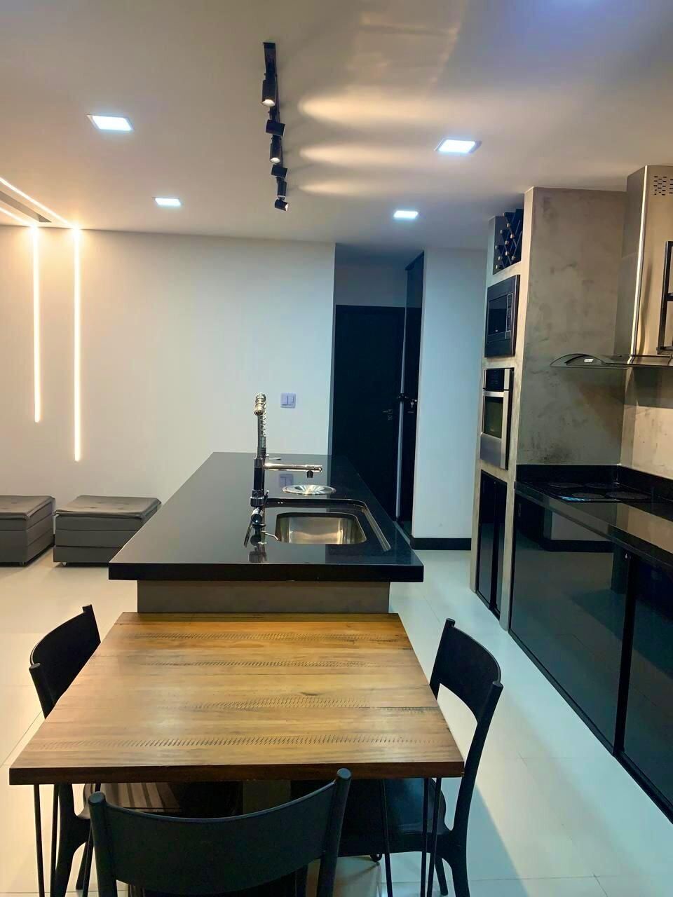 A modern kitchen with a central island, built-in oven, and a dining area with a wooden table and chairs.