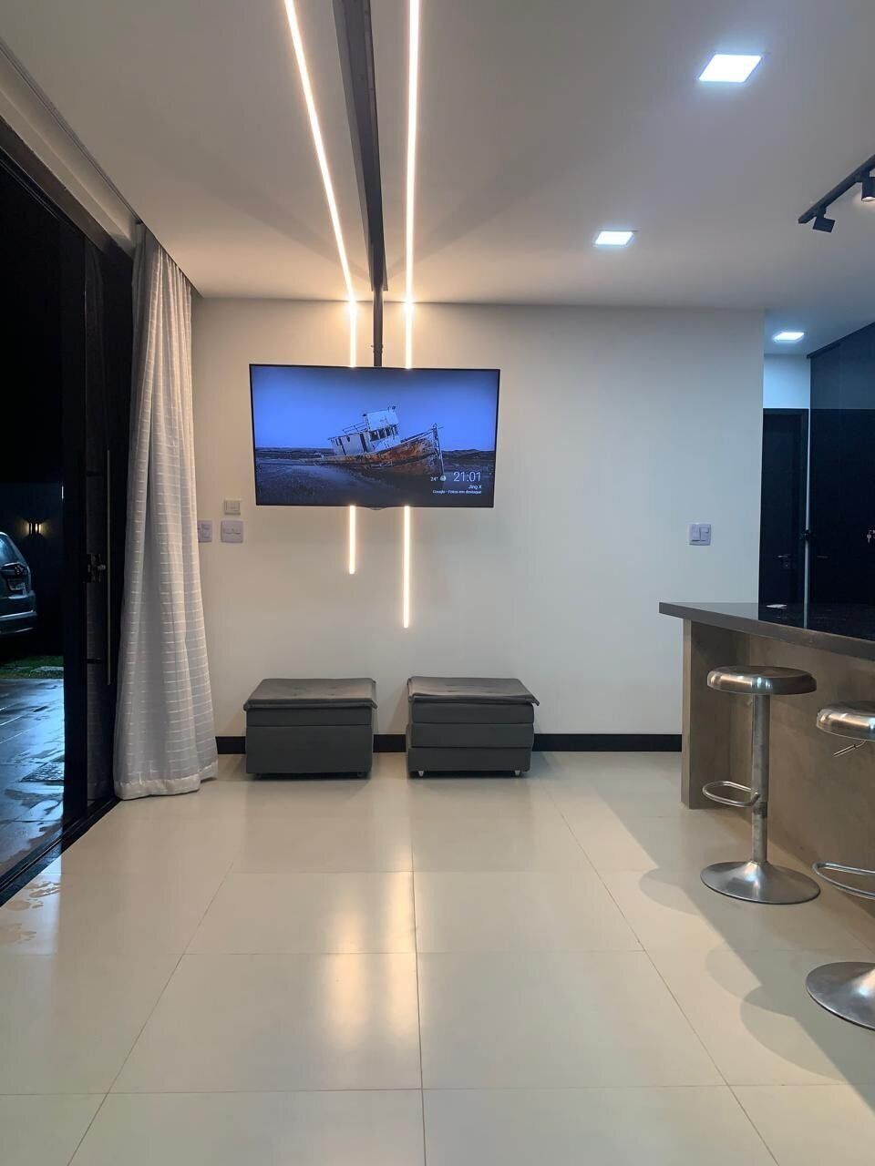 Um hall de hotel moderno com uma televisão de tela plana na parede, uma mesa de recepção e dois pufes.