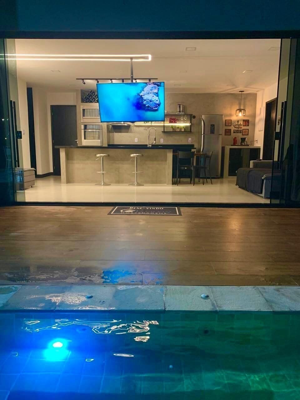 Uma sala de estar moderna com televisão, cozinha e piscina.
