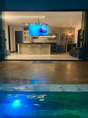 Una sala de estar moderna con televisor, una zona de cocina y una piscina.