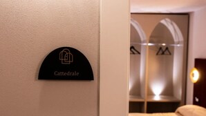 A hotel room with a bed, a wall-mounted sign with the name 'Cattedrale,' and a closet with mirrored doors. - Chiave di Volta Luxury Rooms & Suites (Palermo)