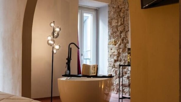 A bedroom with a bed, a bathtub, and a stone wall. - Chiave di Volta Luxury Rooms & Suites (Palermo)