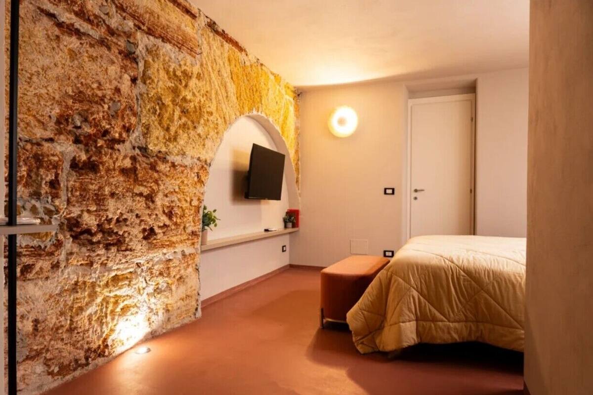 Ein Schlafzimmer mit Stehwand, einem Bett, einem Fernseher und einer kleinen Sitzbank.