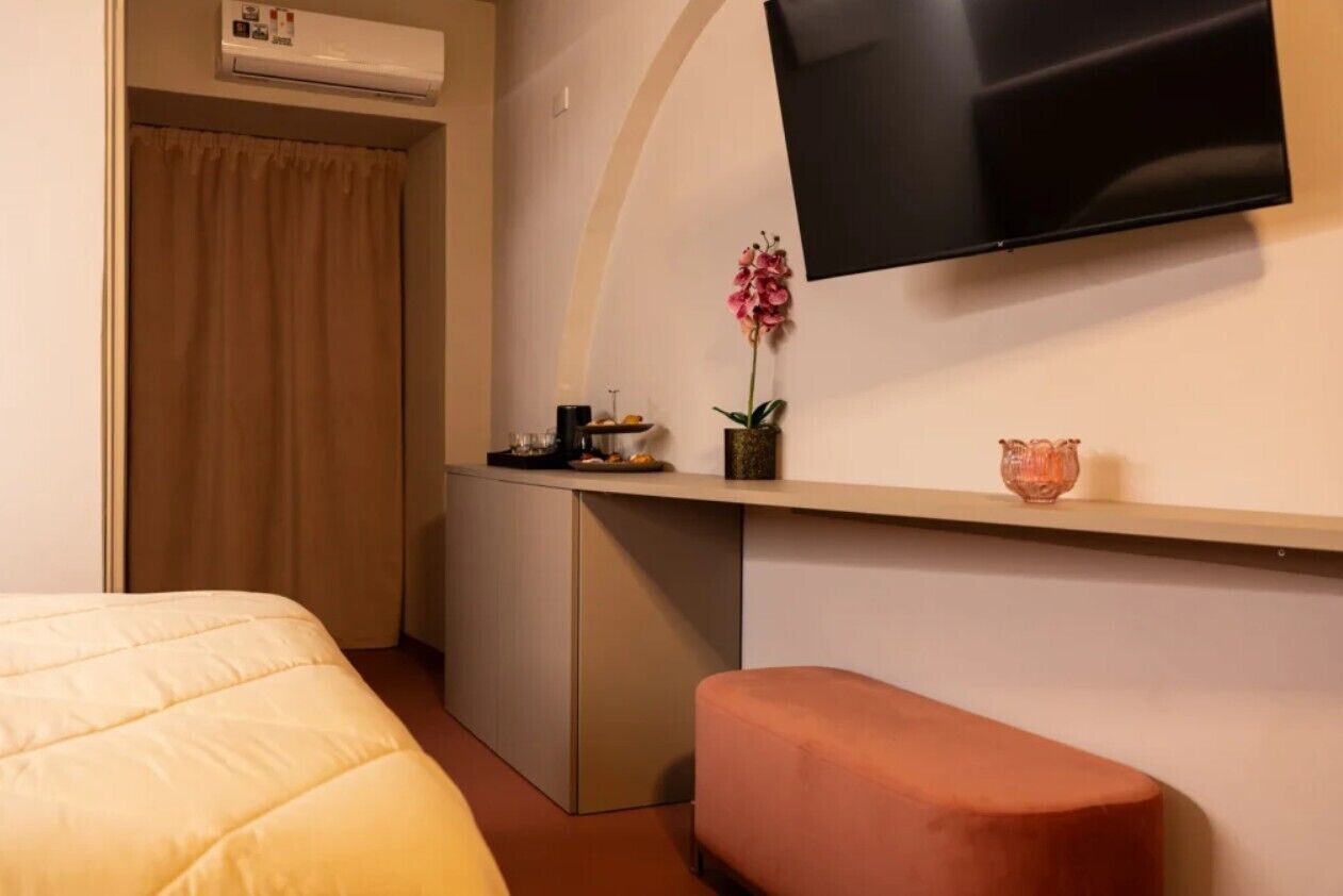 Habitación de hotel con cama, escritorio, televisor, orquídea en maceta y una mesita con objetos encima.