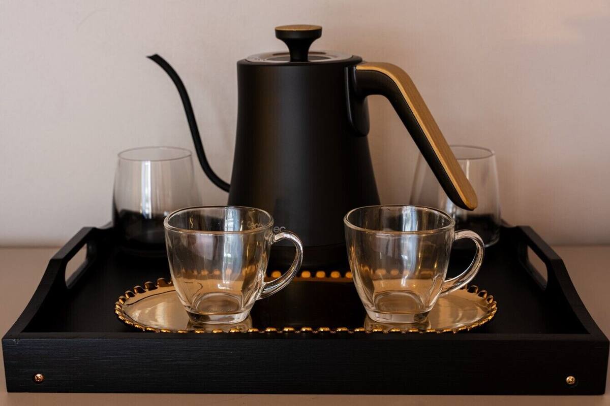 Eine Kaffeemaschine in Schwarz mit goldenem Griff auf einem schwarzen Tablett, zusammen mit zwei transparenten Gläsern.