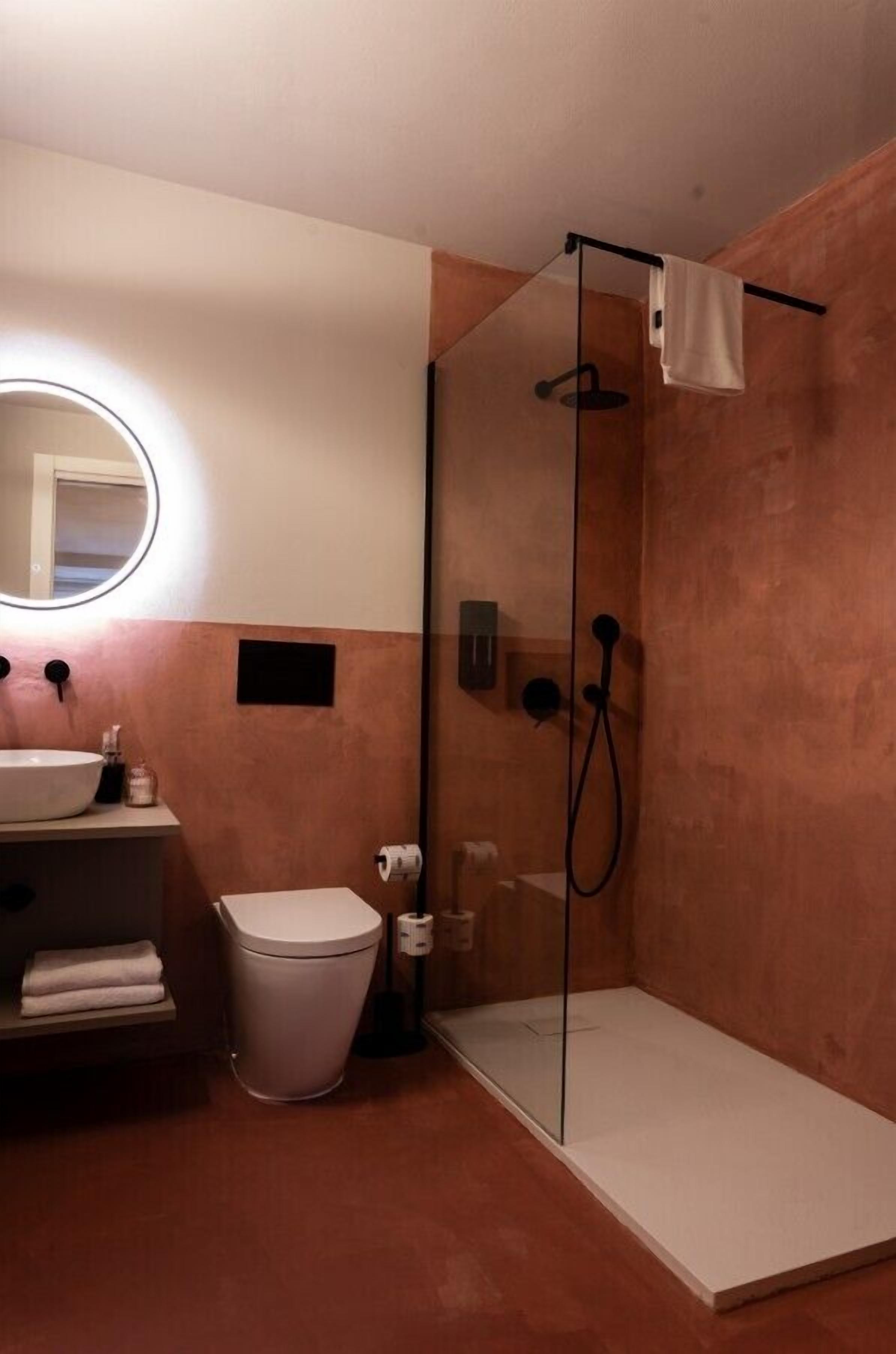 A modern bathroom with a glass-enclosed shower, a round mirror, a sink, and a toilet.