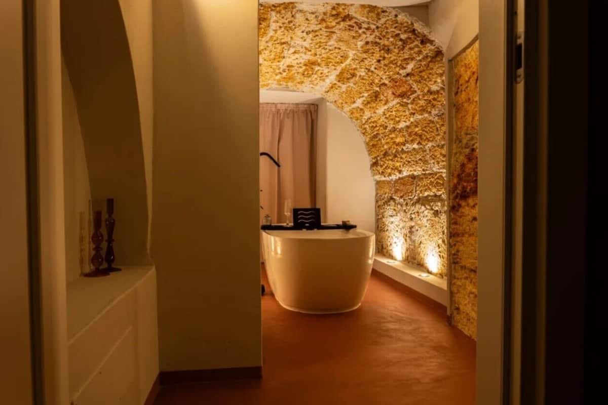 Ein Flur, der zu einem Badezimmer mit Steinwand, einer Badewanne und einem Waschbecken führt.