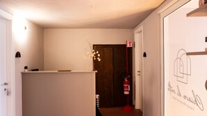 A hallway with a reception desk, a fire extinguisher, and a door with a sign. - Chiave di Volta Luxury Rooms & Suites (Palermo)
