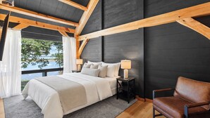 Une chambre à coucher avec un lit, une table de chevet, une lampe, une chaise et une vue sur l’extérieur.