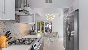 Una cucina moderna con piano cottura a gas, elettrodomestici in acciaio inossidabile e zona pranzo illuminata da un lampadario.