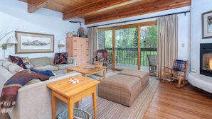 A cozy living room with a wooden ceiling, a fireplace, a sofa set, a coffee table, and a view of the outdoors.