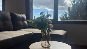 A living room with a sofa, a coffee table with a remote control, and a vase with flowers. - Apartment in Berzosa del Lozoya with beautiful views (Berzosa del Lozoya)
