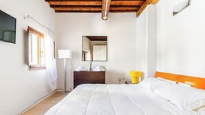 A bedroom with a bed, a bedside table, a mirror, a window with curtains, and a wooden ceiling. - Bright loft with elevator in the historic center of Florence (Firenze)
