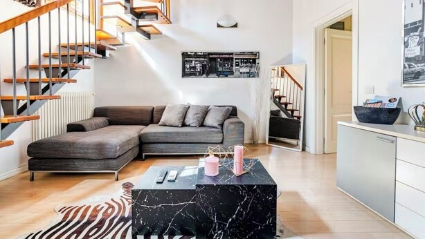 A modern living room with a sofa, a black marble coffee table, a zebra-patterned rug, a staircase, and a kitchen area. - Bright loft with elevator in the historic center of Florence (Firenze)
