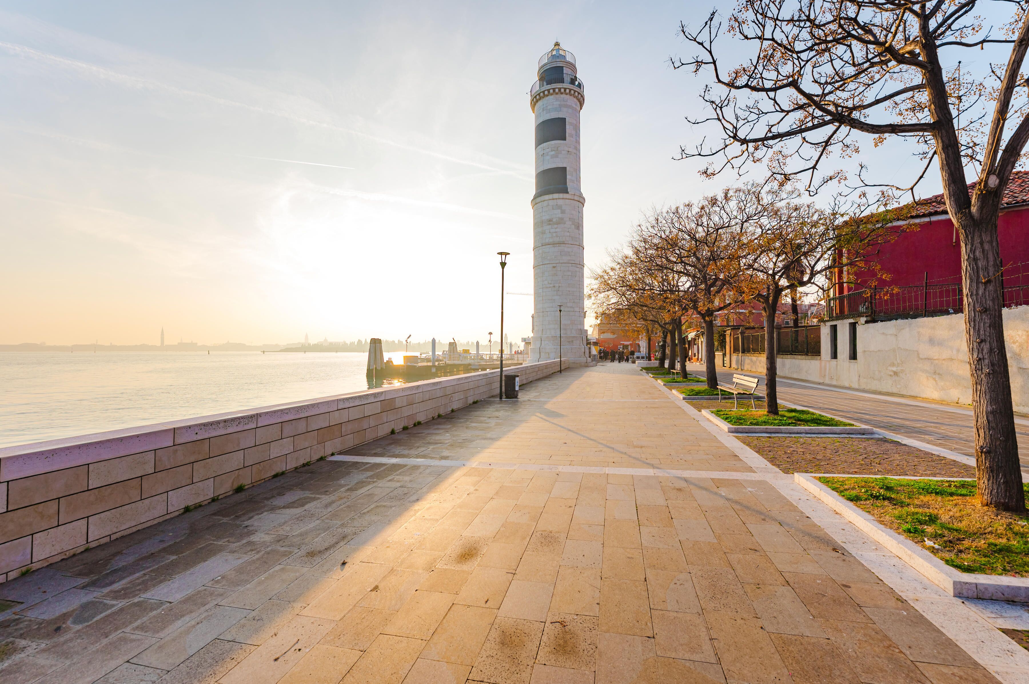 Un paseo marítimo con un faro, un camino de ladrillos y árboles.