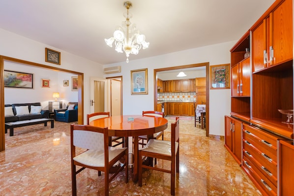 A spacious living area with a dining table, chairs, a sofa, and a kitchen in the background.