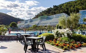 Een hotel met een zwembad, terras en een bergachtig landschap op de achtergrond.
