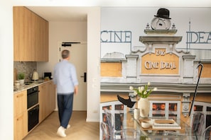 A modern kitchen with wooden cabinets, a coffee machine, and a dining area with a glass table and chairs.