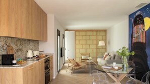 Een moderne keuken met houten kastjes, een marmeren aanrechtblad en een eethoek met een glazen tafel en transparante stoelen.