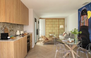 A modern kitchen with wooden cabinets, a marble countertop, and a dining area with a glass table and clear chairs.