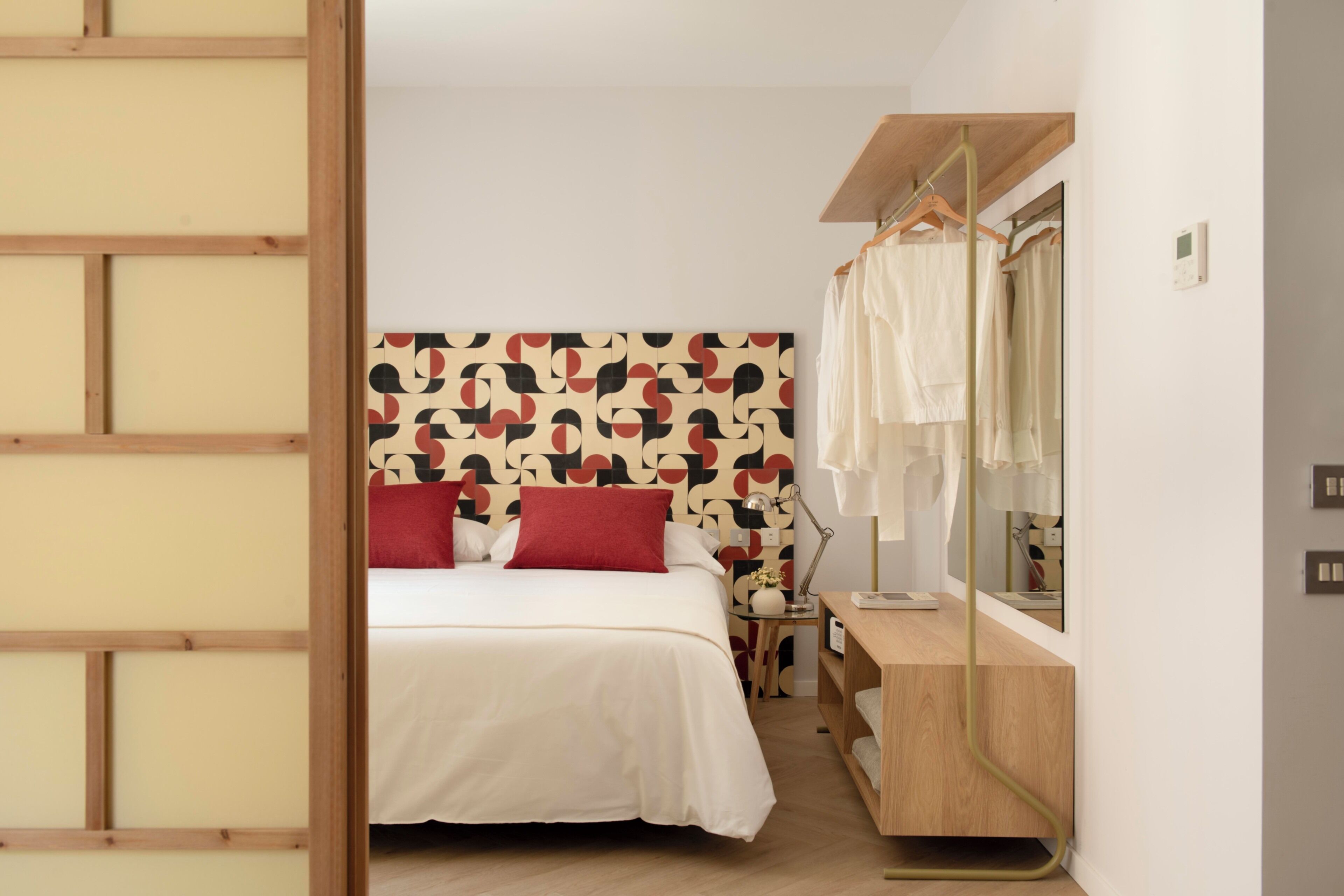 Een slaapkamer met een bed, nachtkastje, spiegel en een muur met een geometrisch patroon.