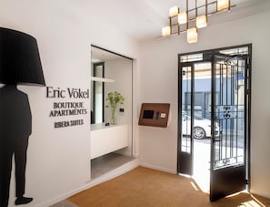 Un intérieur moderne avec un comptoir d’accueil, une enseigne indiquant « Eric Vökel Boutique Apartments », une porte dotée d’un portail métallique et un couloir menant à l’entrée.