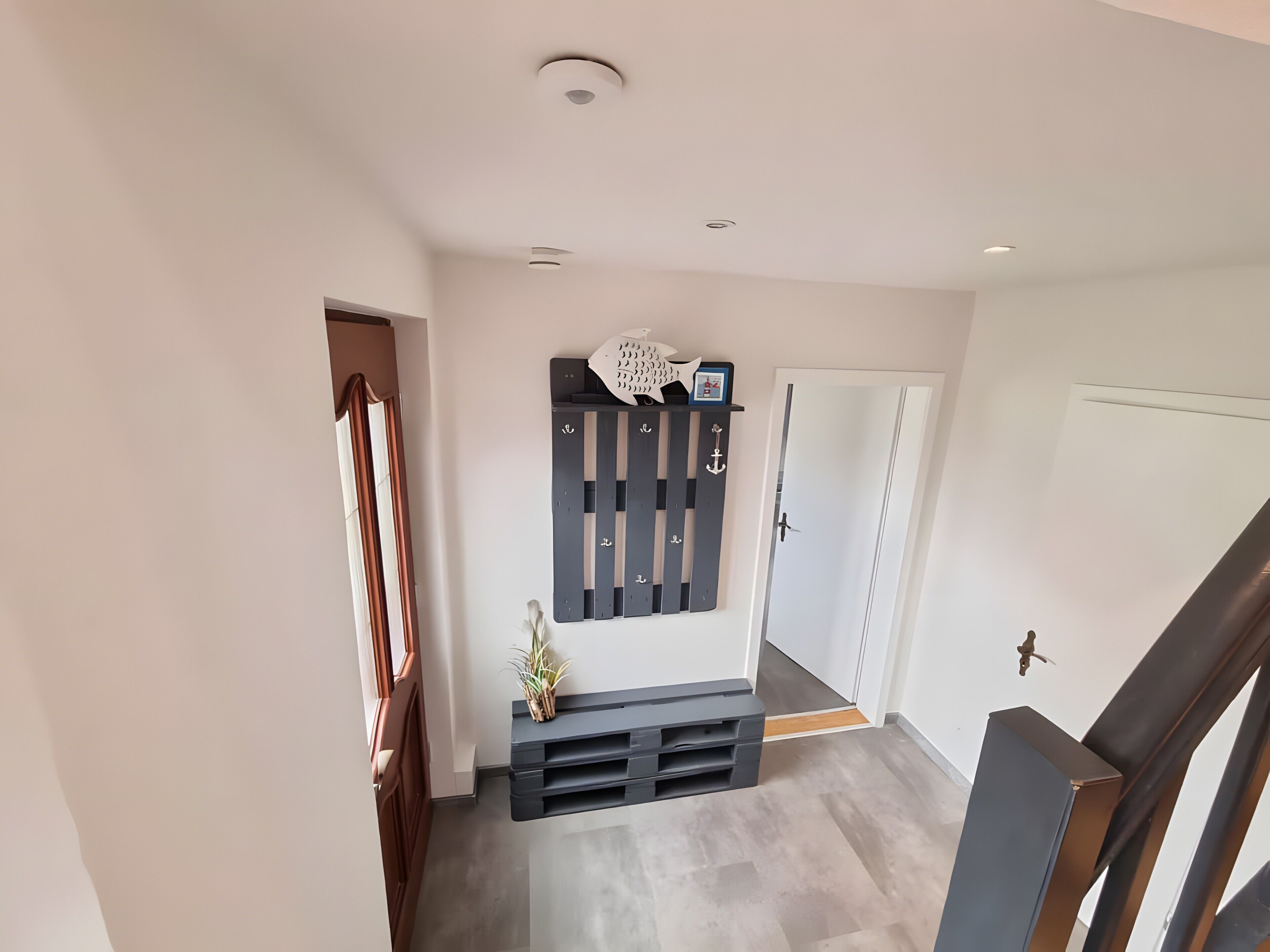 Un couloir avec un banc en bois sombre, un élément décoratif fixé au mur et une porte donnant sur une autre pièce.
