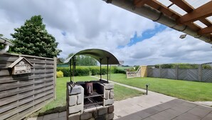 Um quintal com churrasqueira de pedra, cerca de madeira e um pérgola.
