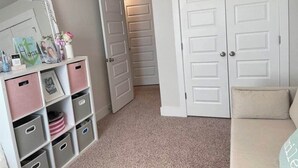 Een kamer met een beigekleurig tapijt, een witte deur, een beigekleurige bank en een witte inbouwkast met spiegel en opbergmanden.