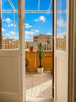 A balcony with a potted cactus, a chair, and a view of a cityscape. - CASA FRIDA, cozy bright attic with terrace. (Roma)