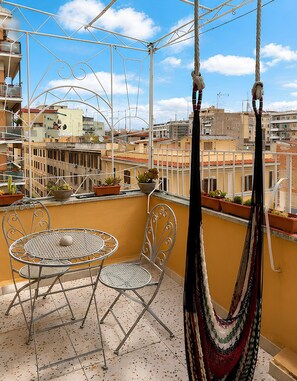 Un balcón con una silla de metal, una mesita y una hamaca.