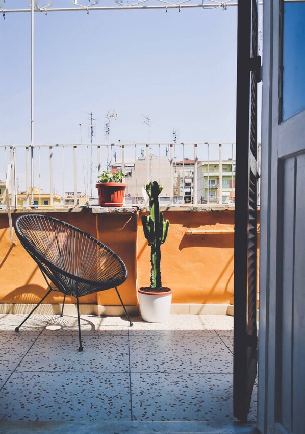 Un balcón con una silla, un cactus en maceta y vistas a edificios.