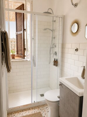 Un baño moderno con ducha envuelta en vidrio, inodoro blanco y lavamanos con grifo dorado.