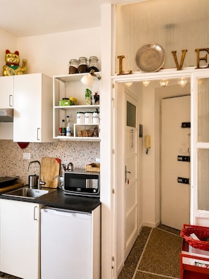 A compact kitchen with white cabinets, a sink, a microwave, and a countertop with a cutting board and utensils. - CASA FRIDA, cozy bright attic with terrace. (Roma)