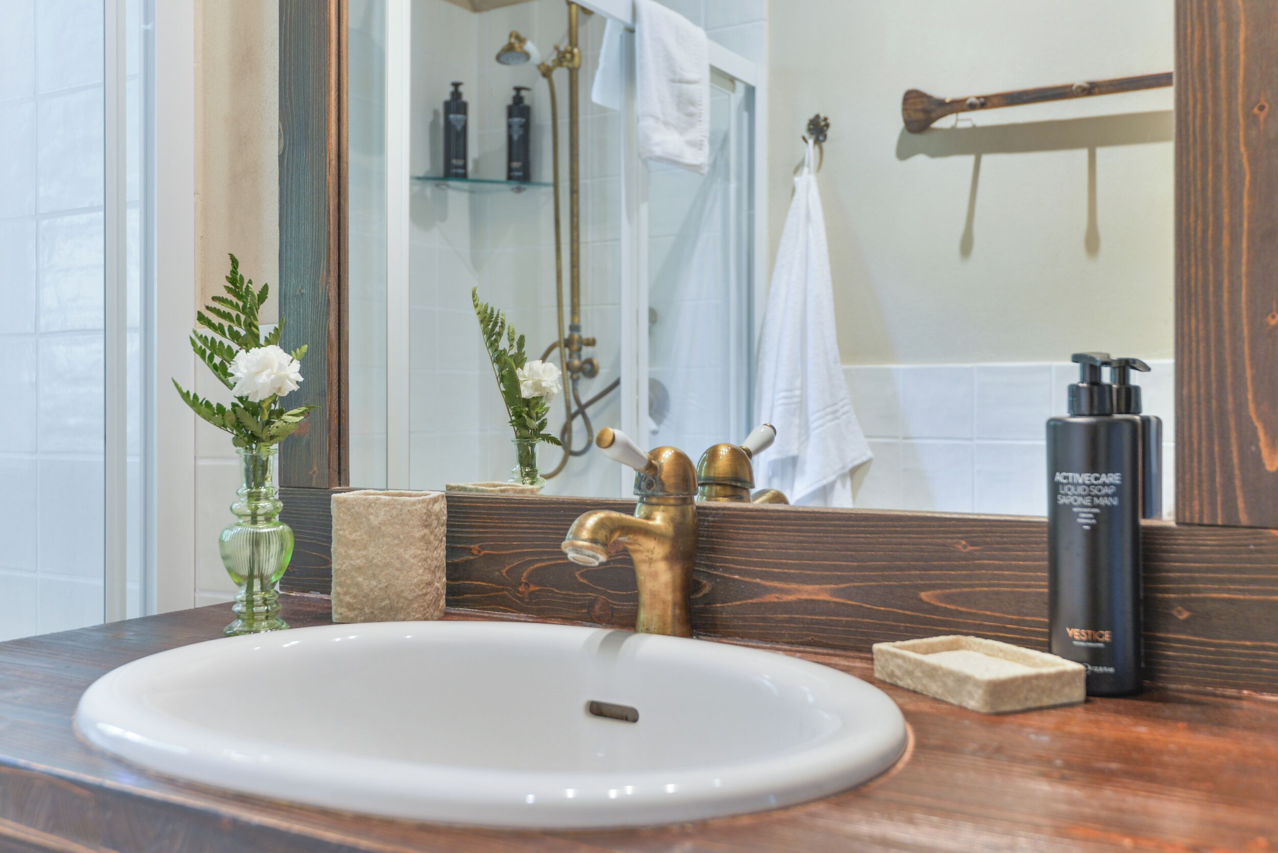 Ein Badezimmer mit einem weißen Waschbecken, einem Messingarmaturen, einem Spiegel und einem Handtuchhalter.
