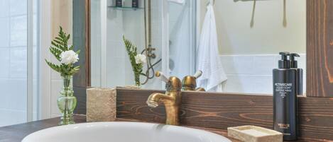 A bathroom with a white sink, a brass faucet, a mirror, and a towel rack.