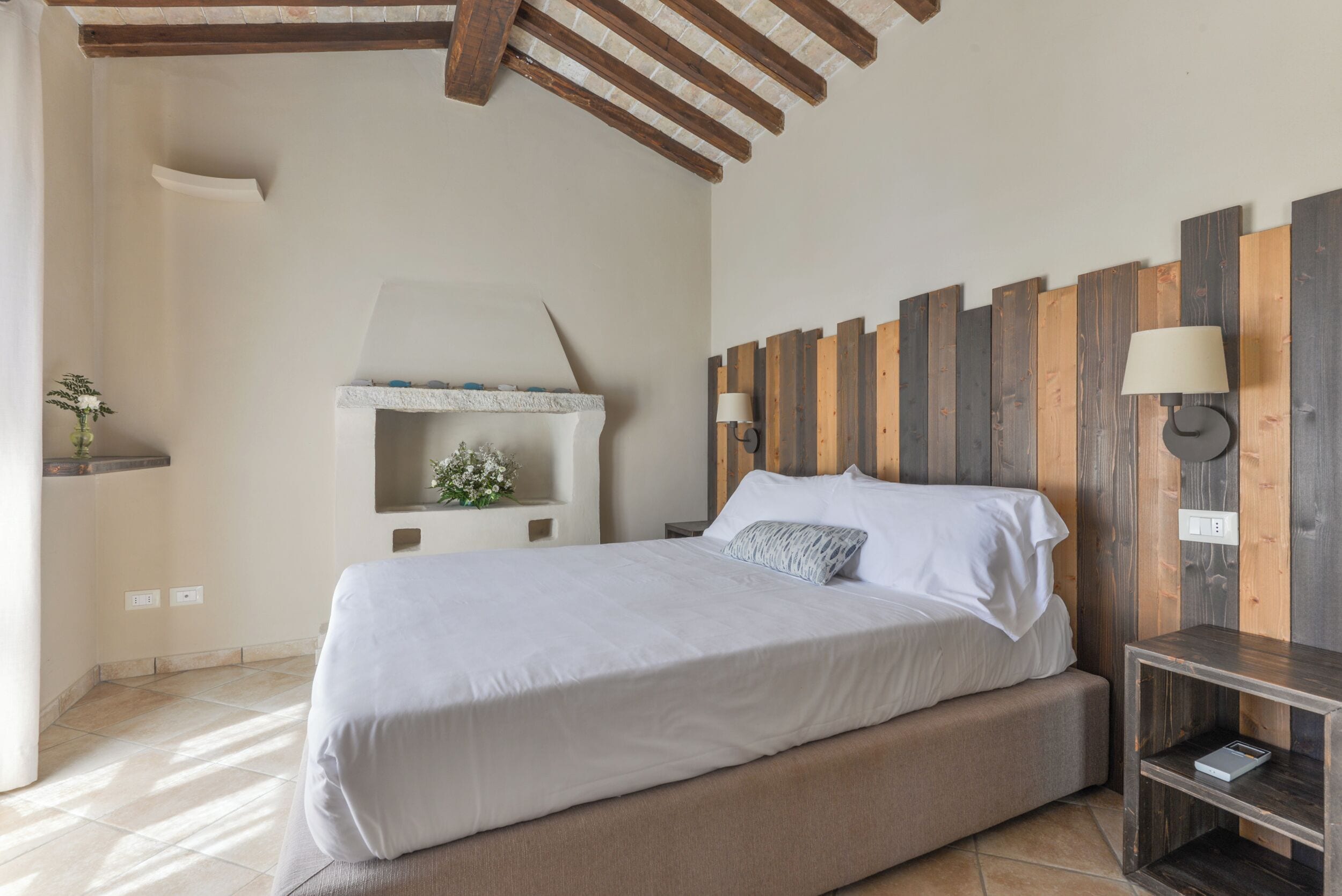 A bedroom with a bed, a nightstand, a wall-mounted lamp, a shelf with a plant, and a wooden headboard.
