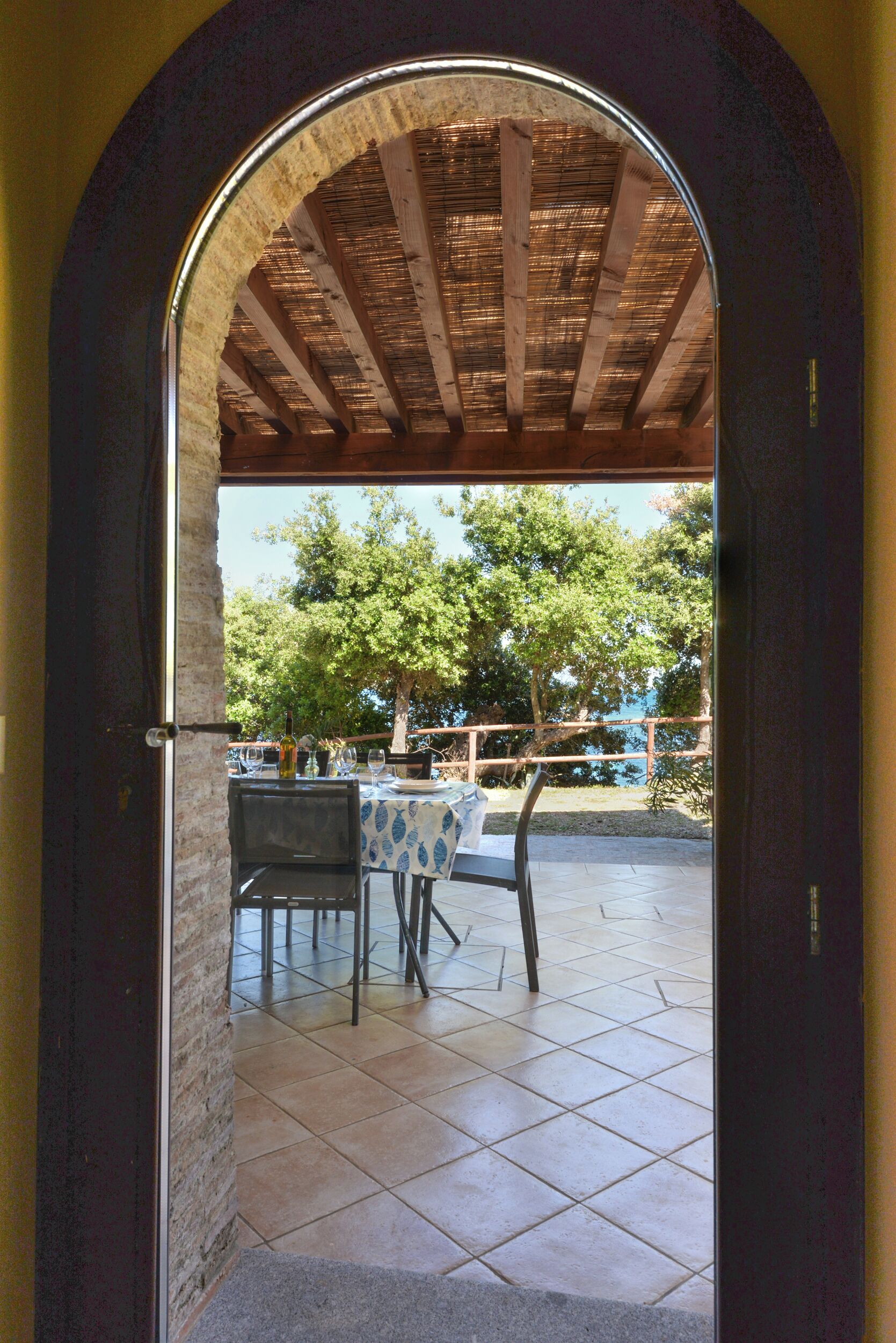 An arched doorway leading to an outdoor patio with a table and chairs, a wooden ceiling, and a view of trees.