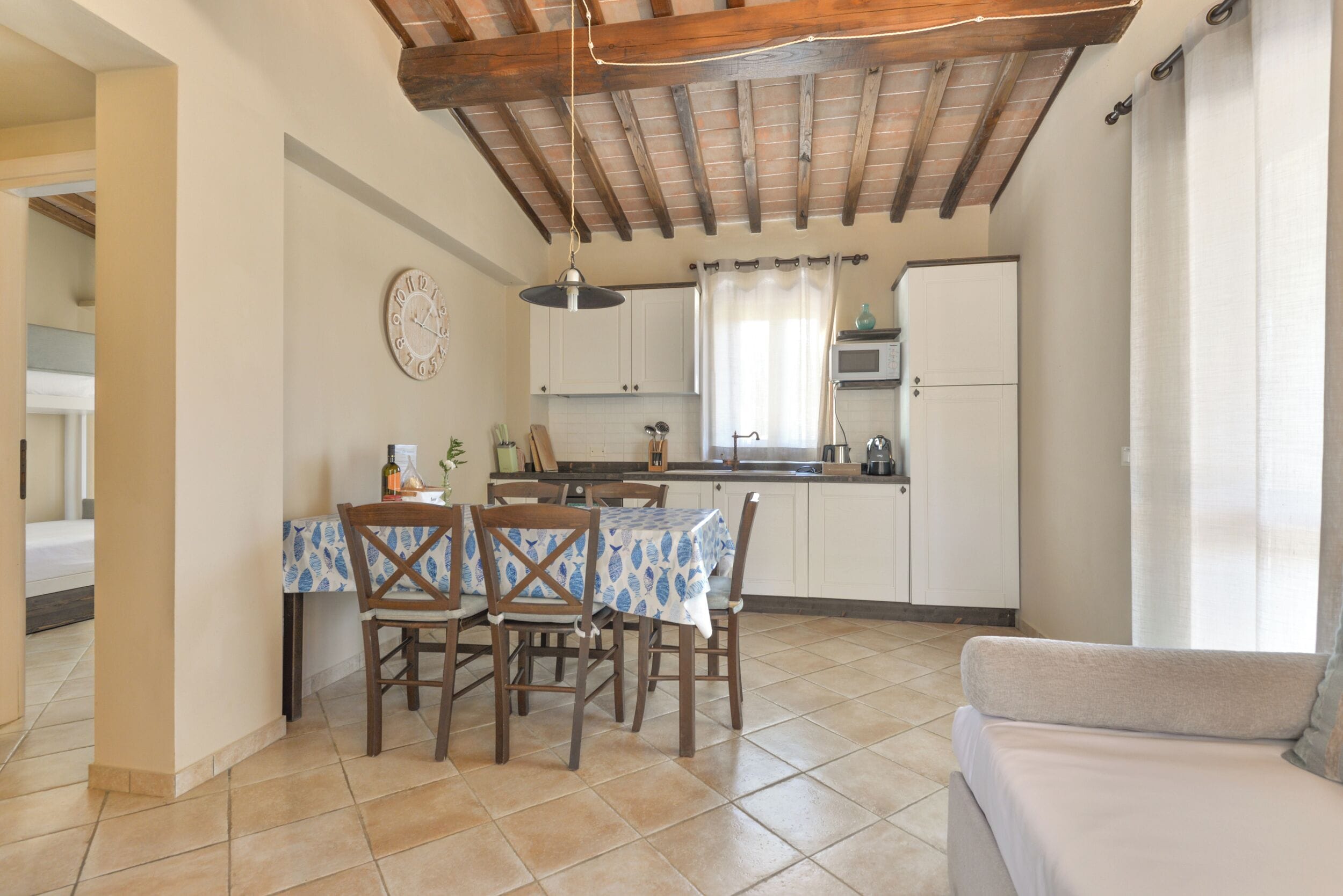 A kitchen with a dining table, chairs, a clock, and a refrigerator.