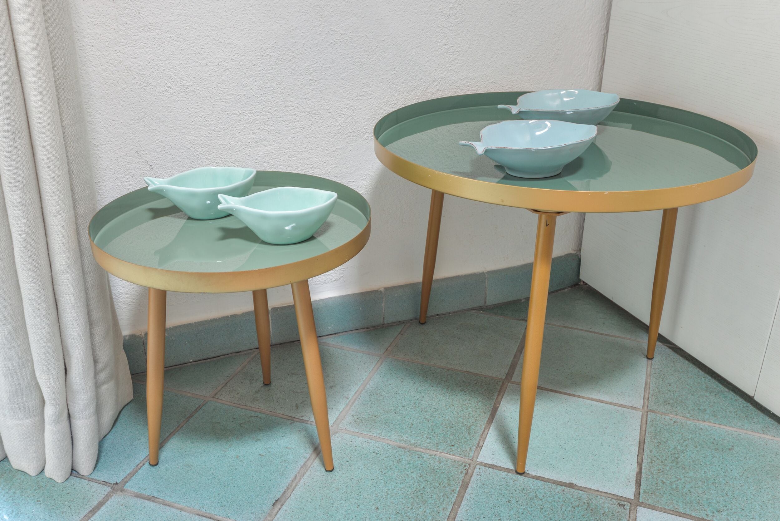 Two glass-top tables with wooden legs, each with a light blue bowl on top.