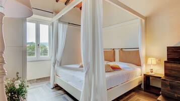 Ein Bett mit Himmelbett, ein Nachttisch mit Lampe und Blick ins Freie durch ein Fenster.